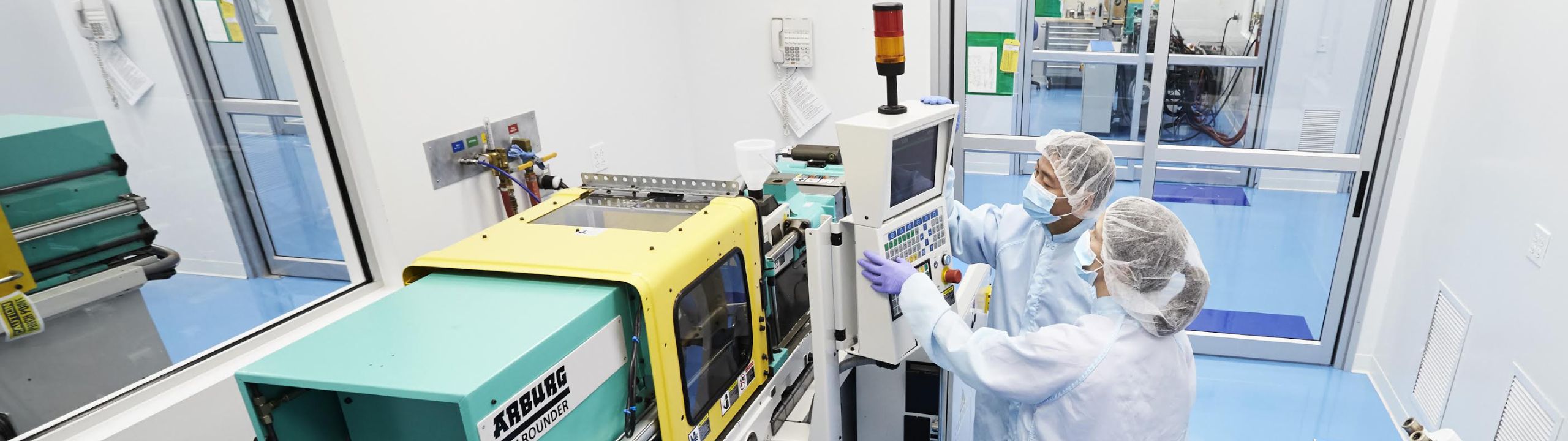 Contract Manufacturing Two Technicians In Laboratory Gear Stand In Front Of The Console Of A Large Machine