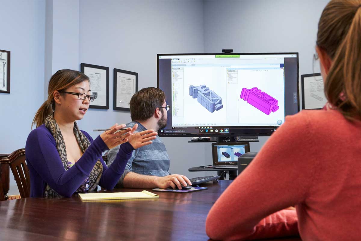 Bioabsorbable Device Part Design A Woman Motions With Her Hands And Talks To Colleagues In A Meeting In Front Of A Screen Showing Cad Like Drawings Of A Bioabsorbable Product